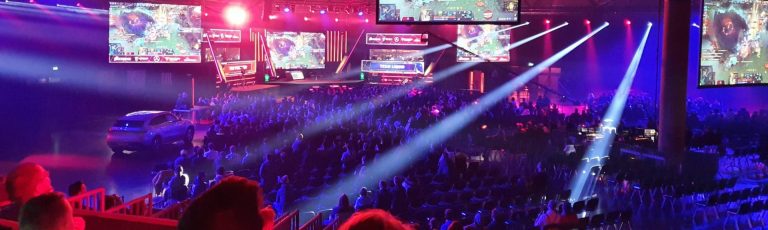 Eine große Halle mit vielen Menschen die alle auf verschiedene Bildschirme blicken. Es wird das Videospiel Leauge of Legends gespielt.